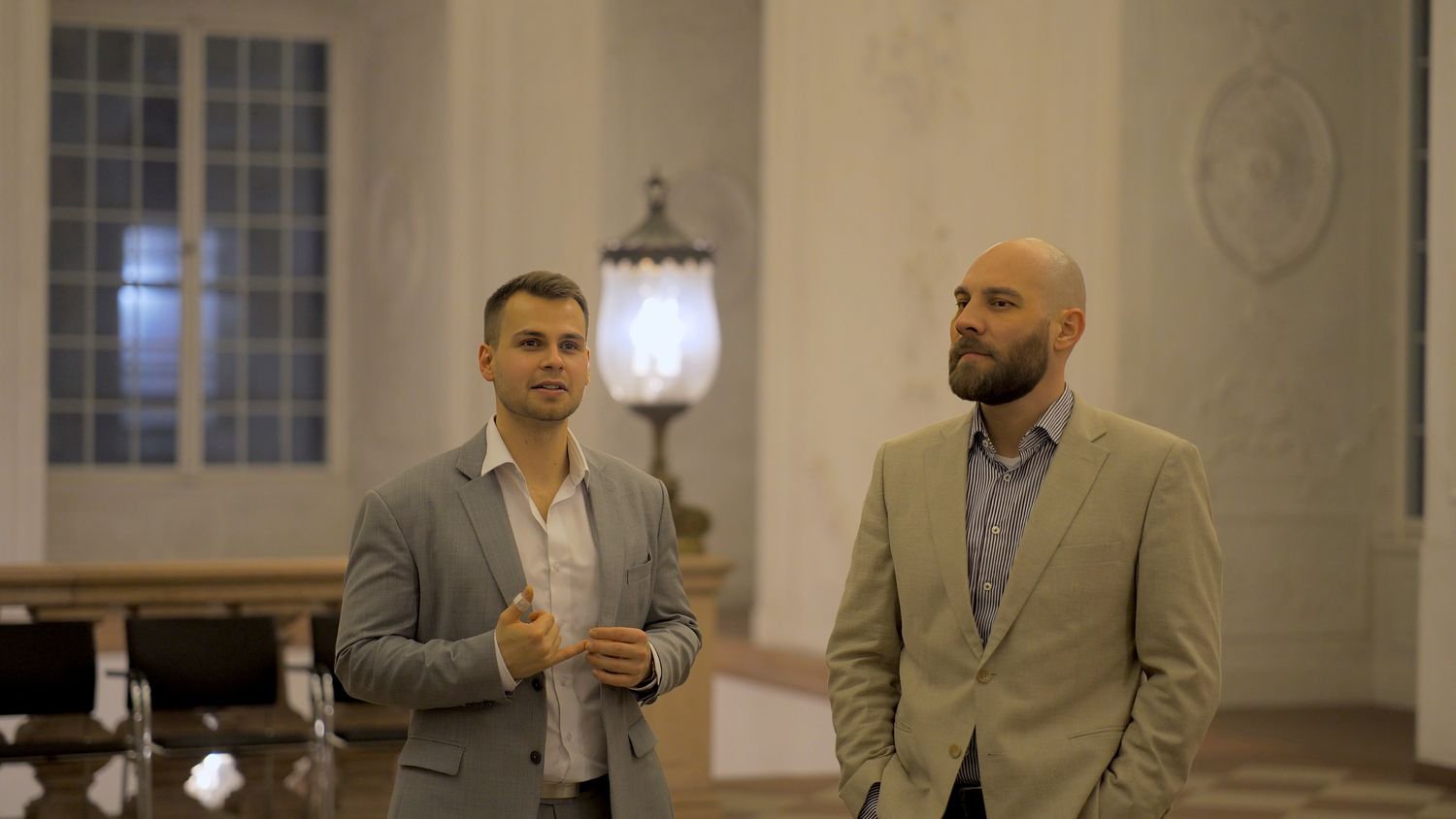 Zwei Personen im Gespräch in einem hellen Saal, eine erklärt gestikulierend etwas.